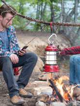Load image into Gallery viewer, Pictured in metallic red for the open swivel hook and silver for the rest of the clip is a medium-sized metal carabiner hooked to a tree branch and holding aloft a red metallic lantern emitting a yellowish white light. This is a HeroClip Medium in Hot Rod Red. Perfect for your roof top tent adventure camp tool hanging needs! Available for sale in other colours (but not this colour) by SMRT Tent in Edmonton, Canada.