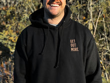 Load image into Gallery viewer, Pictured from their moustache down to their torso is a male model wearing our Get Out More. Hoodie in Black. With this close-up we can distinguish a wavy sort of texture from the hoodie's fabric. The background is a forest in spring or early fall. Chill out around your SMRT Tent roof top tent or get out more by hiking in this cozy hoodie! Available for sale by SMRT Tent in Edmonton, Canada.