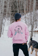 Load image into Gallery viewer,  Pictured from the knees up, a male model with his back facing the camera is wearing a SMRT Pink Skeleton Crewneck. The back view depicts an enlarged version of our White laughing skeleton above and overlapping a mountain range with two simple pine trees in Black to its right (our left) and the words Stay Adventurous written in Black above the image. 2 parts of the mountain range are shaded by a baby blue, mimicking snow or daylight. This Crewneck is available for sale by SMRT Tent in Edmonton, Canada.