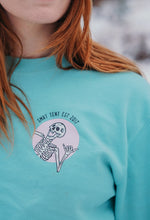 Load image into Gallery viewer, Pictured is a close-up view on our ginger-haired model, showing the laughing skeleton printed on the upper-left chest area of her SMRT Tent Stay Adventurous Skeleton Crewneck in Teal. This Crewneck is perfect to bring along on your overland roof top tent camping adventure! Available for sale by SMRT Tent in Edmonton, Canada.