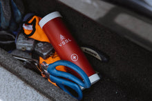 Load image into Gallery viewer,   Pictured in a vehicle's glove box is the packed, compact VSSL First Aid Mini surrounded by miscellaneous items like the pair of scissors with blue-gripped handles. Perfect for your roof top tent camping or hiking first aid needs! Available for sale by SMRT Tent in Edmonton, Canada.