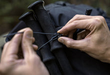 Load image into Gallery viewer, Pictured in black is an adjustable rubber zip tie. There is a pair of hands adjusting the toggle on the zip tie to securely fasten their gear to their backpack or bag. This is a zip tie from a Re-Ties Reusable Zip Ties 4-Pack. Perfect for your overland hiking gear managing, bundling, attaching, fastening and tying needs! Available for sale by SMRT Tent in Edmonton, Canada.