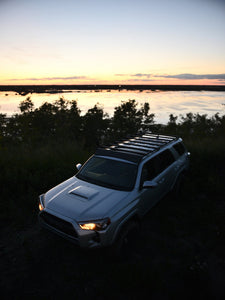 Pictured in the darkening late evening light is a silver Toyota SUV, specifically a 5th Gen 4Runner with the assembled 10-20 4Runner 5th Gen Modular Roof Rack on the car roof. The perfect fit and most compatible choice of modular roof rack for your Toyota 4Runner 5th Gen SUV! Available for sale by SMRT Tent in Edmonton, Canada.