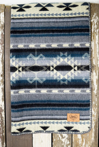 Pictured is a dark blue, grey-blue, black, ice and white coloured, traditional Aztec patterned baby blanket. This is the Heartprint Threads 'Dream Big Little One' Baby Blanket, created by Ecuadorian Artisans. Perfect for your everyday soft & warm baby blanket needs! Available for sale at SMRT Tent in Edmonton, Canada.