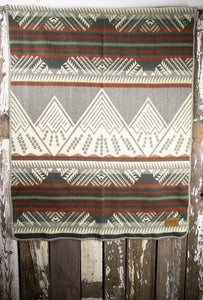 Pictured is a red, grey, dark grey, pale green and white coloured, mountain patterned baby blanket. This is the Heartprint Threads 'Little Climber' Baby Blanket, created by Ecuadorian Artisans. Perfect for your everyday soft & warm baby blanket needs! Available for sale at SMRT Tent in Edmonton, Canada.