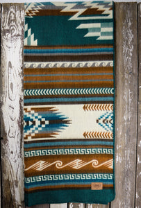 Pictured is a dark teal, blue & brown, wave-patterned and laid-out blanket. This is the Heartprint Threads 'Country Roads' Maskuy Collection Queen Blanket, created by Ecuadorian Artisans. Throw this warm blanket over your sleeping bag while camping outdoors! Available for sale at SMRT Tent in Edmonton, Canada.