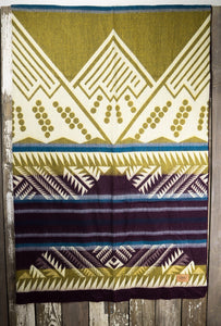 Pictured is a yellow, wine-maroon-magenta, blue & cream, mountain-patterned and laid-out blanket. This is the Heartprint Threads 'Indefatigable' Mountain Flakes Line Queen Blanket, created by Ecuadorian Artisans. Throw this warm blanket over your sleeping bag while camping outdoors! Available for sale at SMRT Tent in Edmonton, Canada.