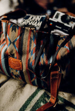 Load image into Gallery viewer, Pictured is a dark blue, light blue, black, terracotta brown, tan and brown patterned bag (similar looking to a duffle bag) with soft, brown leather straps. The bag’s zipper is open and showing its packed insides. This is the Heartprint Threads &#39;Cartagena 2.0&#39; Weekend Traveller Bag, created by Ecuadorian Artisans. Perfect for all your week-long packing, storing and travelling needs! Available for sale at SMRT Tent in Edmonton, Canada.
