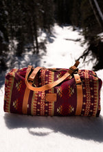 Load image into Gallery viewer, Pictured is a dark red, cherry red, cream, light brown, orange, burgundy, beige and dark golden-yellowish tan patterned bag (similar looking to a duffle bag) with soft, orangey-brown leather straps. This is the Heartprint Threads &#39;Okanagan 2.0&#39; Weekend Traveller Bag, created by Ecuadorian Artisans. Perfect for all your week-long packing, storing and travelling needs! Available for sale at SMRT Tent in Edmonton, Canada.
