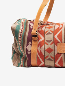 Pictured is a maroon, light tan, beige, brown, dark reddish brown, cream, teal, and orange patterned bag (similar looking to a duffle bag) with soft, orangey-brown leather straps. This is the Heartprint Threads 'Two Jack' Weekend Traveller Bag, created by Ecuadorian Artisans. Perfect for all your week-long packing, storing and travelling needs! Available for sale at SMRT Tent in Edmonton, Canada.