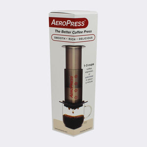 Pictured is a tall, white package that has an image of a clear, grey cylinder with the name AeroPress written lengthwise in red on its side. This is the portable Original AeroPress Coffee Press. Perfect for your overland roof top tent coffee, espresso and cold brew maker needs! Available for sale by SMRT Tent in Edmonton, Canada.