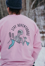 Load image into Gallery viewer, Pictured from the waist up, our male model is with his back facing the camera. This back view gives a closer look at our White laughing skeleton with a mountain range and two simple pine trees to its right (our left) and the words Stay Adventurous written in Black above the image. This Pink Skeleton Crewneck is available for sale at SMRT Tent in Edmonton, Canada.
