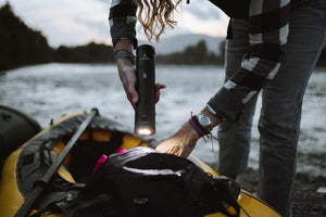 Pictured is a model with only their legs and arms in frame. They are bent over a yellow single-person boat/kayak in which lies a bag. They are holding our packed Black cylinder's flashlight end and shining it downwards. Perfect for your hiking, camping or rowing supply needs! Available for sale by SMRT Tent in Edmonton, Canada.