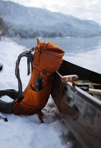 Pictured is an orange camping or hiking bag with it's front leaning against a boat/canoe. and its left side facing the camera. In the side pocket facing us is the Black packed VSSL Camp Supplies. Perfect for your hiking, camping or rowing supply needs! Available for sale by SMRT Tent in Edmonton, Canada.