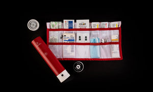 Pictured is the red cylinder with an unrolled red multi-pocket strip filled with medical items on the right, and the top end cap is unscrewed, revealing it is also a compass. This is the unpacked VSSL First Aid kit. To the right of the open red cylinder and below the unrolled multi-pocket first aid kit is a tin and 20 foot roll of Adventure Tape. Perfect for your roof top tent camping first aid kit needs! Available for sale by SMRT Tent in Edmonton, Canada.