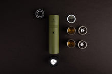 Load image into Gallery viewer, Pictured is the olive green cylinder, showing the top end cap to be a compass and laying just above and to the left. The flashlight end cap is unscrewed and set down in front of the cylinder. On the right side are two lines of items. The first, downward: the bottle opener, the two un-collapsed metal shot glasses. The next line: the two lids for collapsed shot glasses. Perfect for your roof top tent camping spirit needs! Available for sale by SMRT Tent in Edmonton, Canada.

