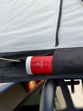 Load image into Gallery viewer, Pictured is a close-up view of an outside side pocket from a light grey, completely set-up softshell roof top tent. This is “The” Softshell, a roof top tent perfect for all overland roof top tent family outdoor camping! Available for sale by SMRT Tent in Edmonton, Canada.

